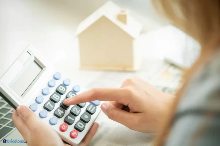 Une femme fait un calcul avec une calculatrice devant une maison miniature.